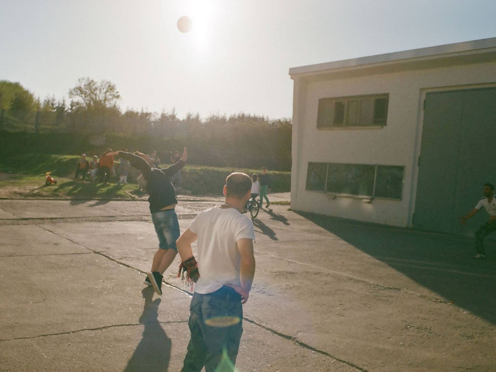 Männer, die auf einem Hof Ball spielen und weitere Erwachsene und Kinder im Hintergrund.
