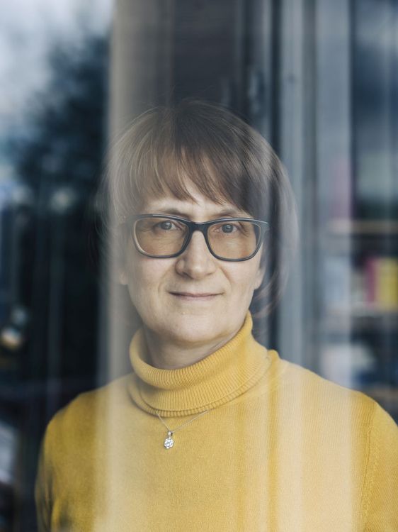 Svetlana Berdyugina schaut durch eine Scheibe in die Kameralinse. Sie trägt einen gelben Rollkragenpullover und eine Brille. 
