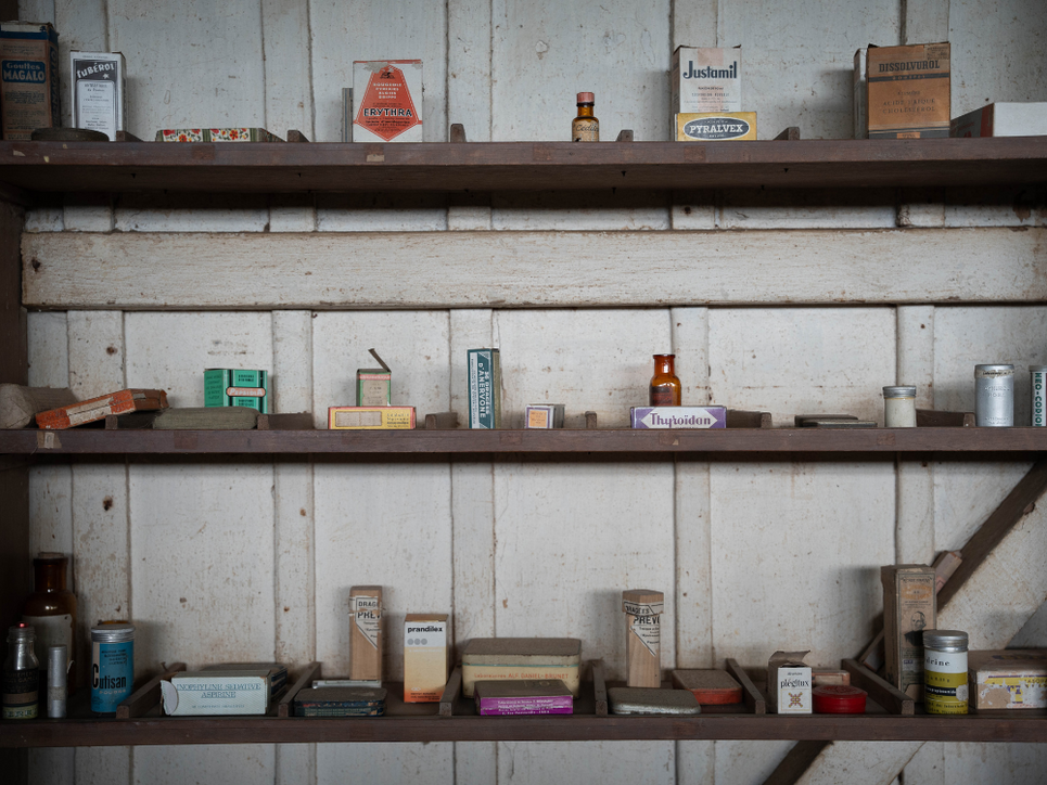 Foto aus dem historischen Krankenhaus von Schweitzer. Drei Regalbretter gefüllt mit Medikamenten in alten Verpackungen.