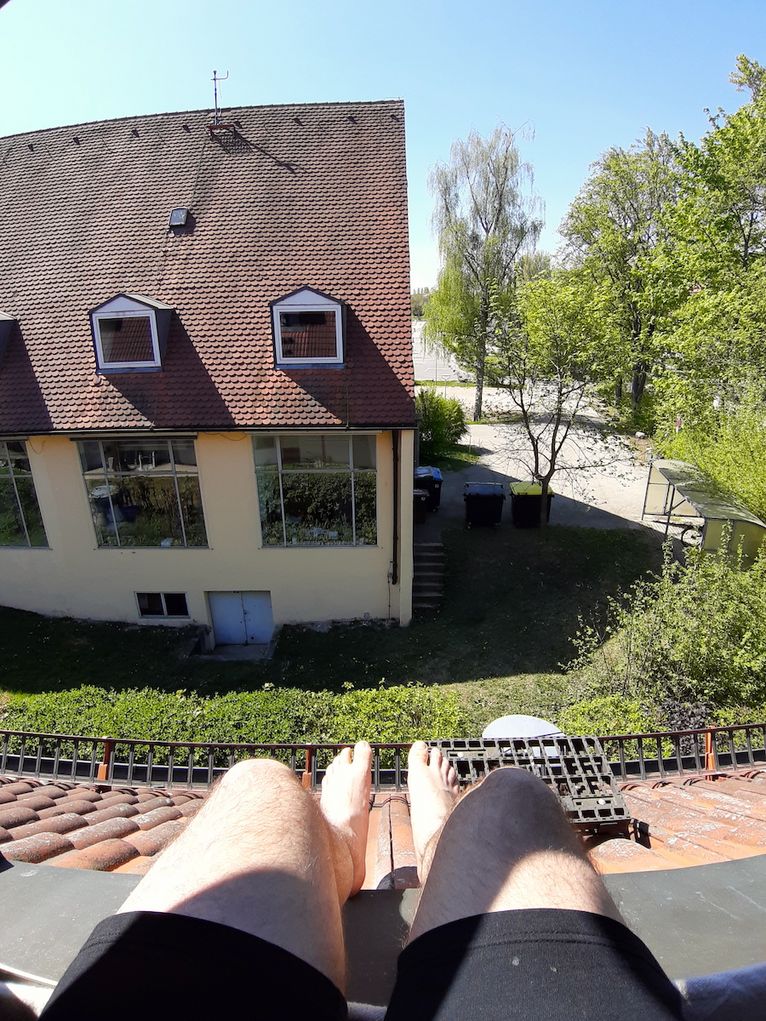 Beine in Shorts baumeln vom Dachfirst eines Hauses, Blick auf ein anderes Haus.
