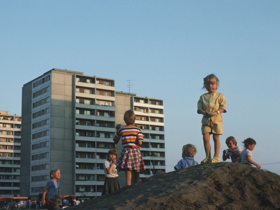 Kinder auf einem kleinen Hügel vor Plattenbauten.