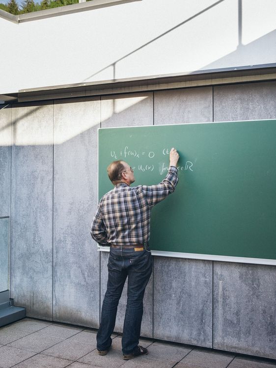 Ein Mann schreibt eine Formel an eine Tafel.