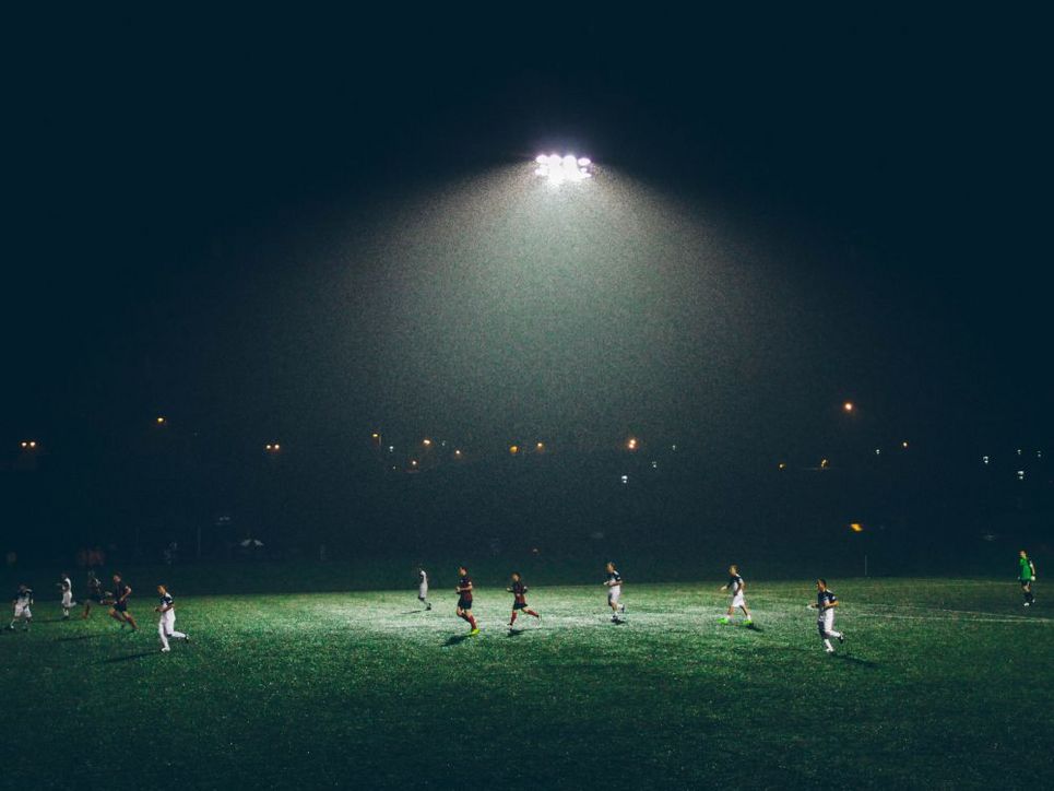 Fußballspieler spielen in dunkler Nacht im Flutlicht.