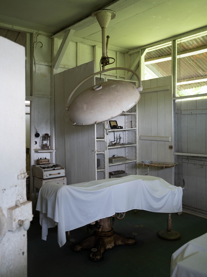 Behandlungsraum des historischen Krankenhauses von Schweitzer. Mittig eine Liege mit weißem Laken. Darüber eine weiße Lampe. Im Hintergrund Holzschränke mit Utensilien.