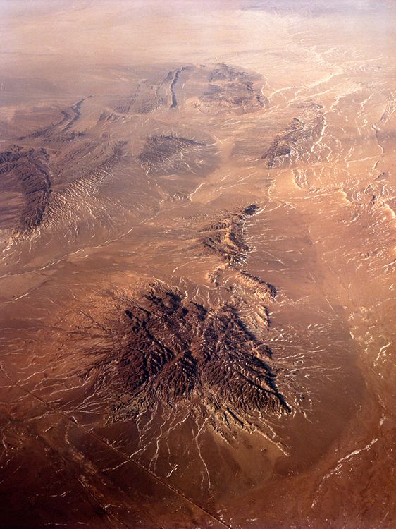 Luftbildaufnahme einer bräunlichen Landschaft, im Vordergrund eine kraterförmige Erhebung