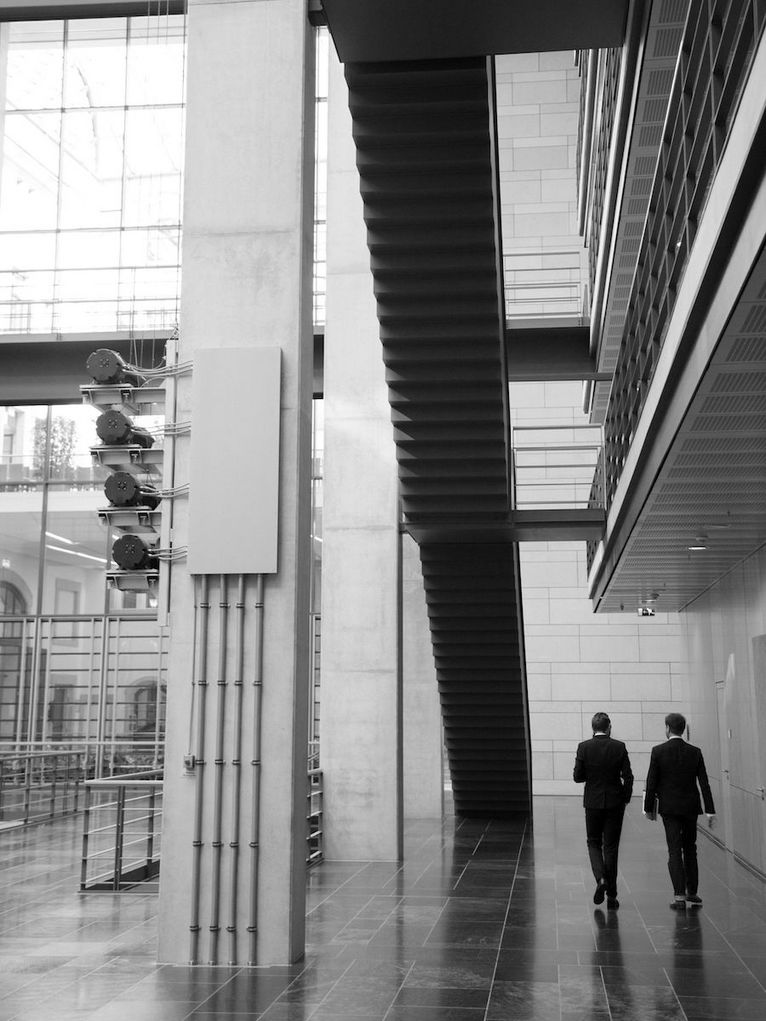 Zwei Personen von hinten in einem Gebäude mit großer Glasfront.