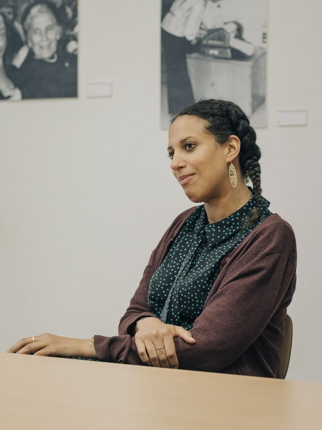 Lisa Höckel sitzt an einem Tisch, an der Wand hinter ihr Schwarzweiß-Fotogrfien.