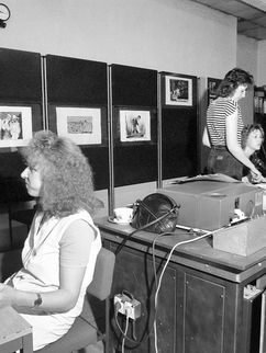 Schwarzweißfotografie von drei Frauen in einem Raum mit alten Computern. Eine von ihnen isst.