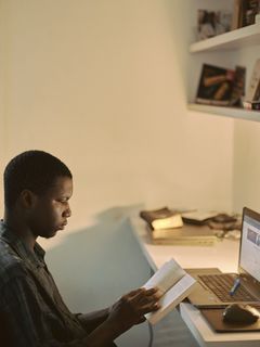 Junger Mann sitzt am Arbeitsplatz mit Buch in den Händen.