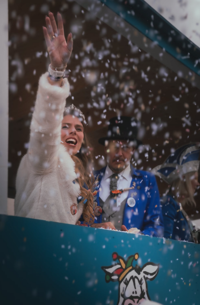 Feiernde Frau beim Karneval-Zug, die winkt und Kofetti fliegt in der Luft.