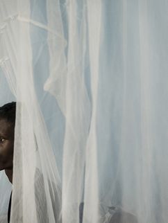 Ein dunkelhäutiger junger Mann blickt hinter einem weißen Vorhang in einer Klinik in Liberia hervor.
