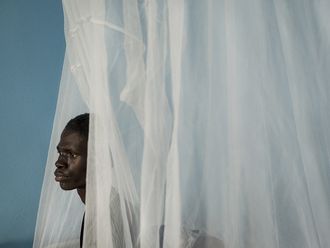 Ein dunkelhäutiger junger Mann blickt hinter einem weißen Vorhang in einer Klinik in Liberia hervor.