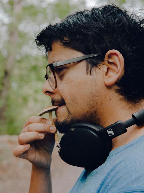 Ein junger Mann mit Kopfhörern um den Hals probiert einen Pilz.