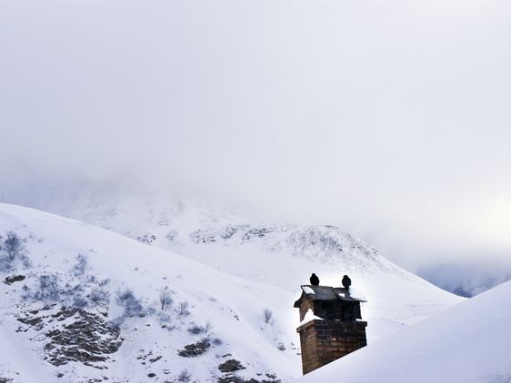 Ein Kirchturm erscheint hinter einem verschneiten Hügel, wolkenverhangener Himmel.
