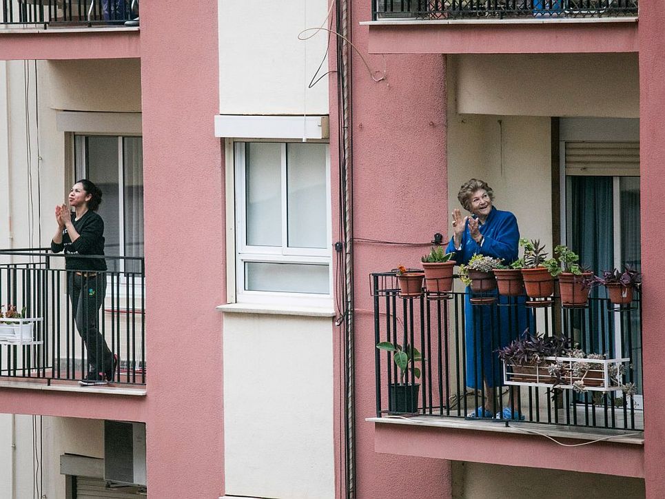 Zwei Frauen, eine ältere und eine jüngere, stehen auf ihren Balkonen und klatschen.