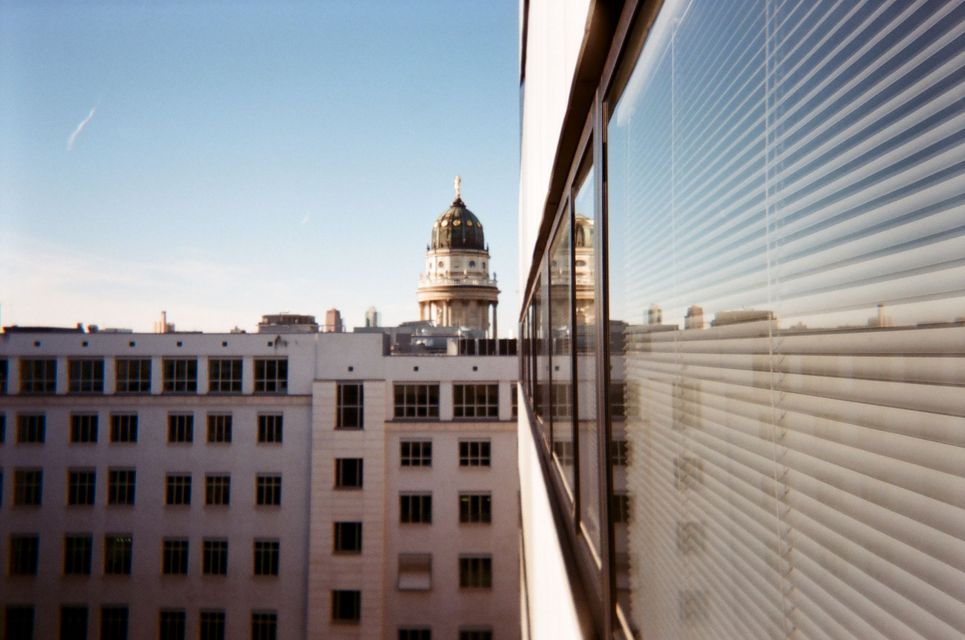 Blick auf eine weiße Fassade mit vielen Fenstern und einem Turm des Frankfurter Tors im Hintergrund.
