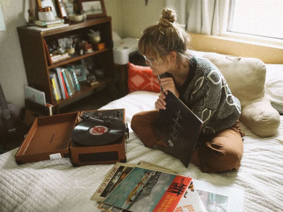 Junge Frau sitzt auf dem Bett mit einem Plattenspieler und Schallplatten.