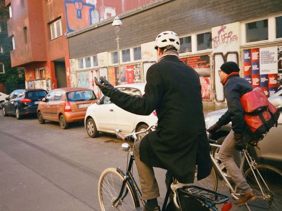 Hanno Hochmuth unterhält sich auf dem Fahrrad mit einer weiteren Person, sie sind von hinten fotografiert und fahren durch die Innenstadt.