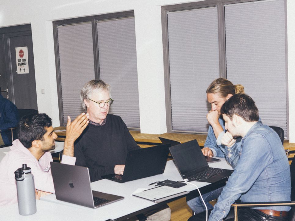 Vier Personen sitzen in einem Raum ohne Tageslicht um einen Tisch vor ihren Laptops.
