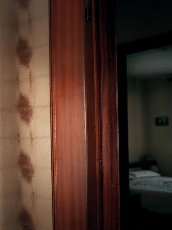 Links im Bild ist eine offene Glastür zu sehen. Durch sie blickt man in ein Zimmer, in dem ein Bett steht.