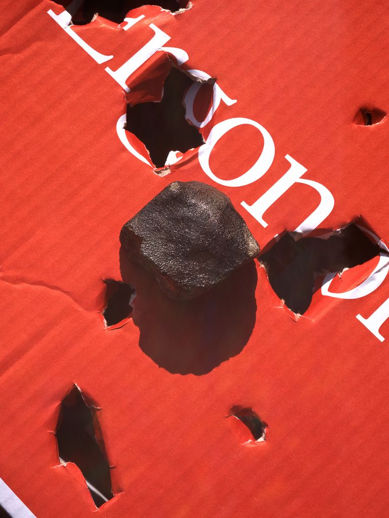 Kleiner, fast schwarzer Meteorit, der Löcher in einem Karton verursacht hat.
