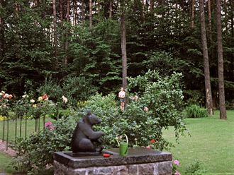 Gartenanlage im Wald mit Rosen, Büschen und der Skulptur eines sitzenden Bären.