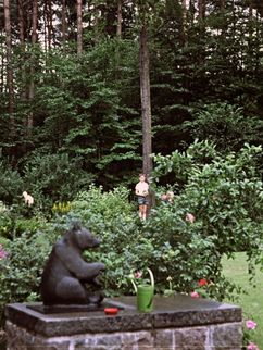 Gartenanlage im Wald mit Rosen, Büschen und der Skulptur eines sitzenden Bären.