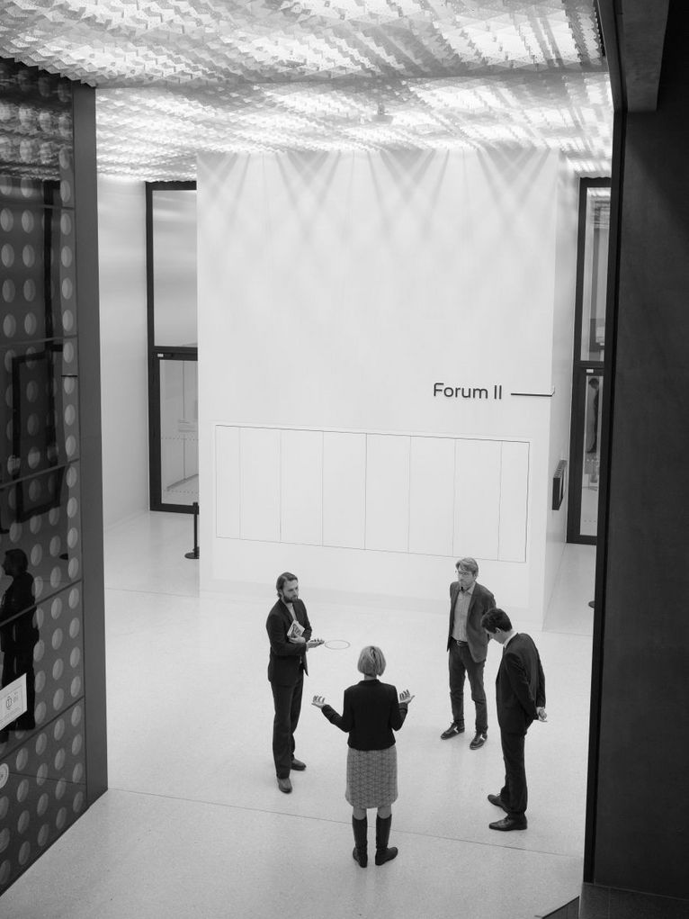Schwarzweißaufnahme von oben: Swen Schulz, Stefan Brandt, Sunhild Kleingärtner und unser Moderator Frank Steinhofer stehen im Forum II  im Futurium, in Berlin. Sie sind im Gespräch.