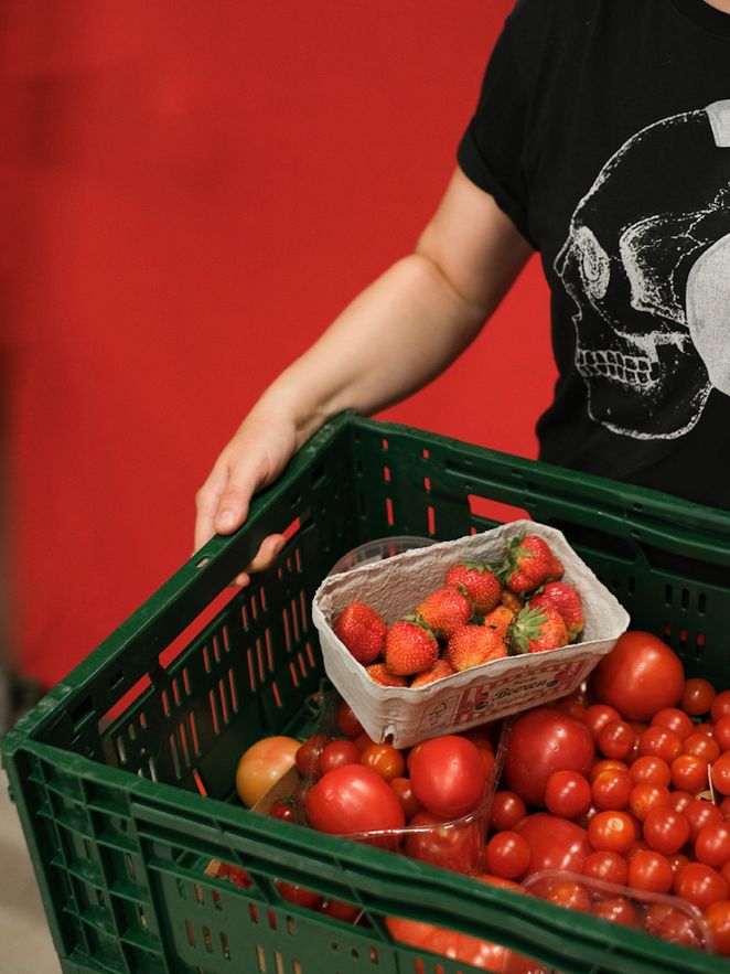 Eine Person trägt eine Kiste voller Tomaten.