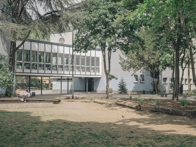 Schulhof mit Bäumen vor einem weiß-grauen Gebäude.