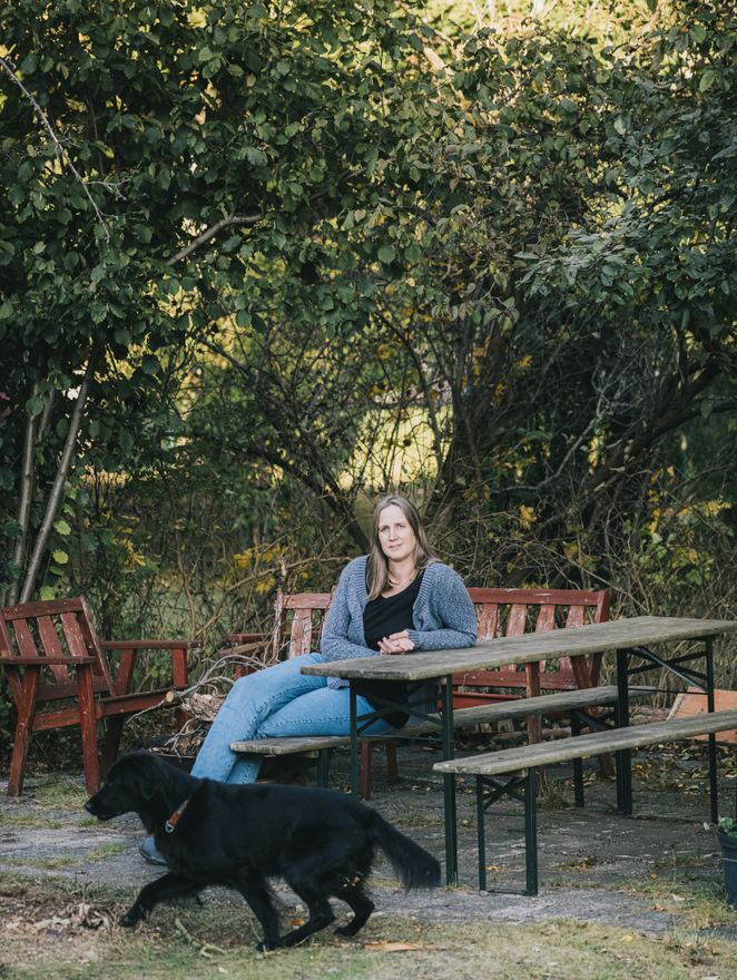 Gesa Kluth sitzt an einem Tisch im Freien, vor ihr läuft ein Hund vorbei.