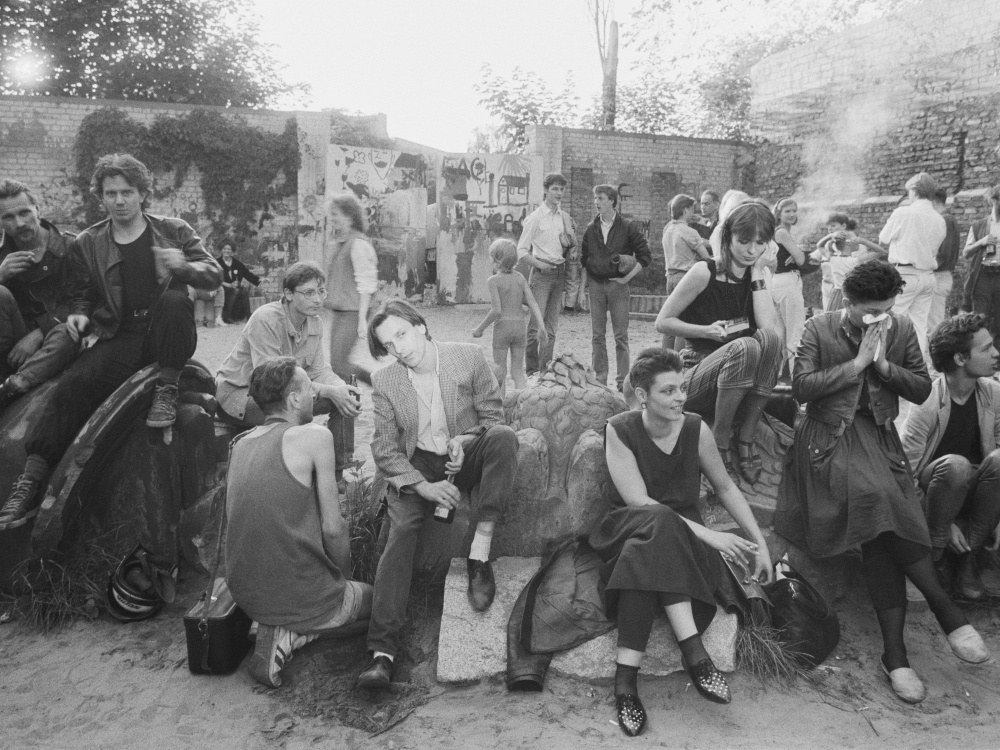Schwarz-weiß Fotografie von vielen jungen Menschen auf einer Ostberliner Brachfläche zur Zeit des Mauerfalls.