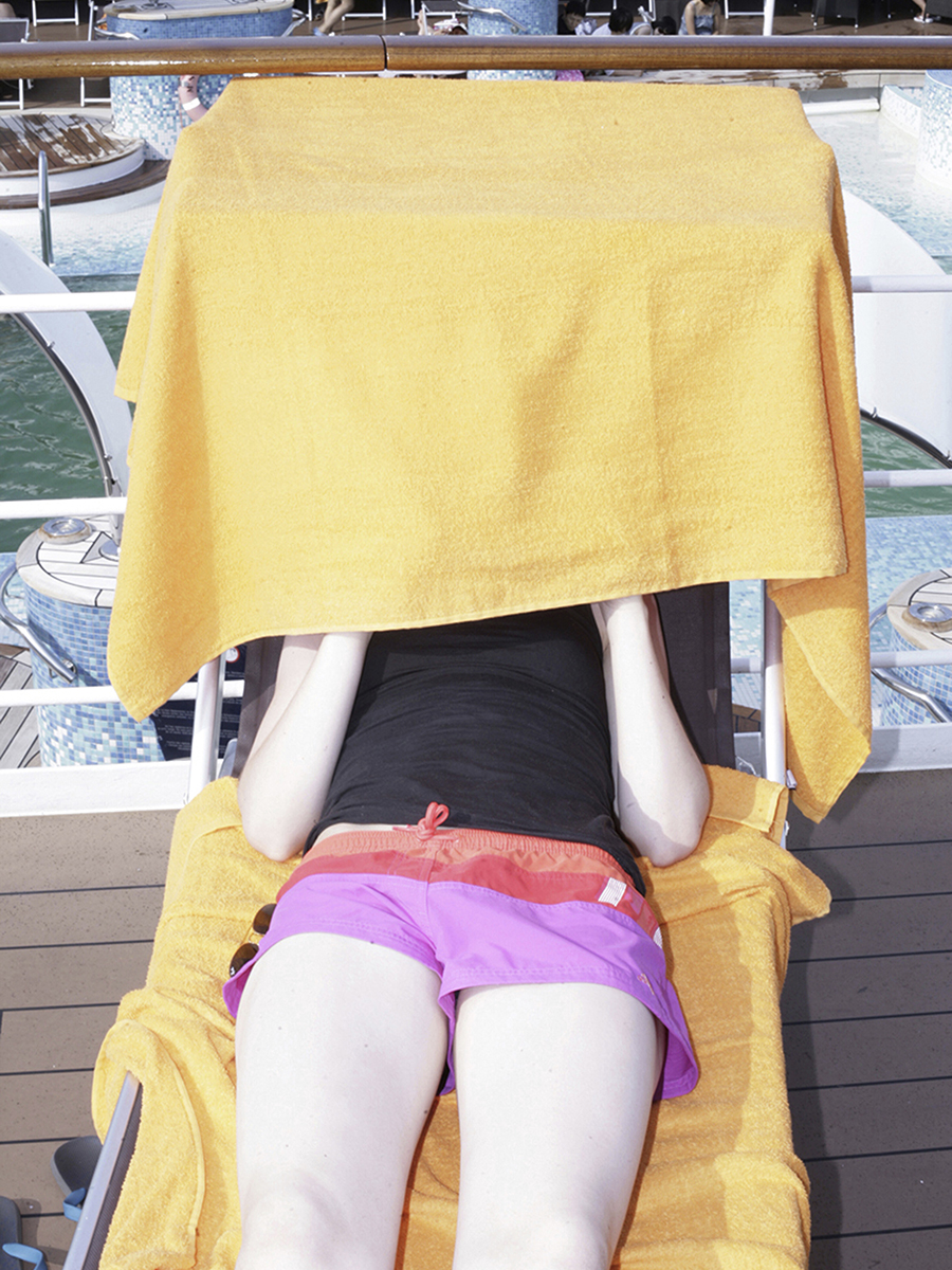 Eine Person sitzt auf einem Liegestuhl, ihr Gesicht ist von einem Handtuch verdeckt.