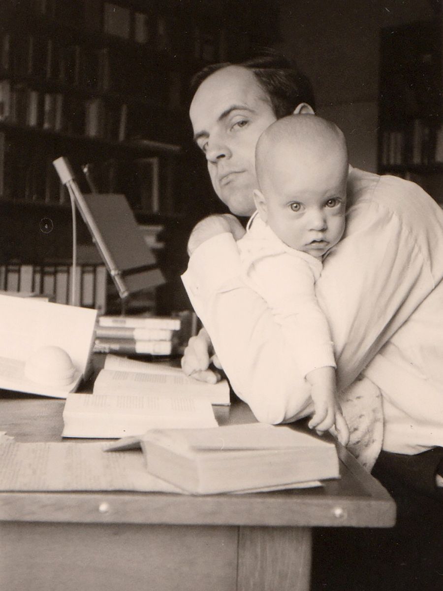Eberhard Knobloch mit einem kleinen Kind auf dem Arm am Schreibtisch.