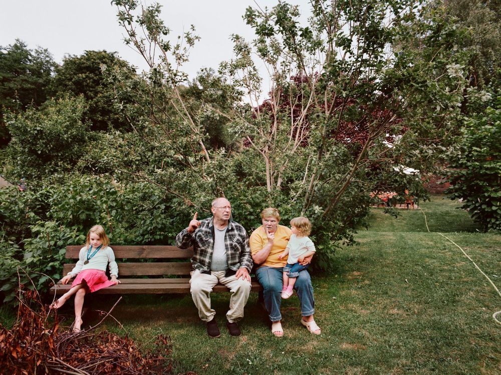 Eine ältere Frau und ein älterer Mann auf einer Bank in einem Garten mit zwei kleinen Mädchen.