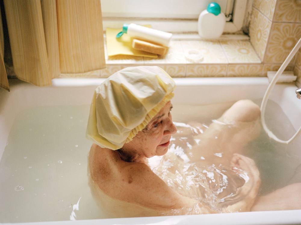 Eine alte Frau mit Badehaube in der Badewanne.