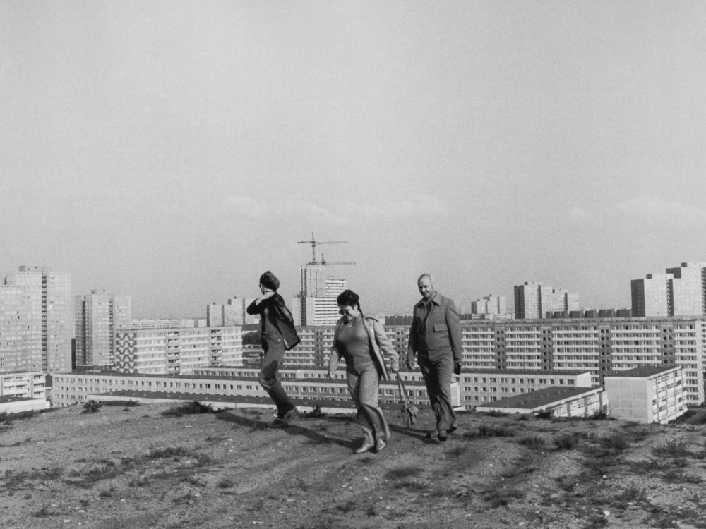 Drei Personen auf einem Hügel vor einer Plattenbausiedlung.