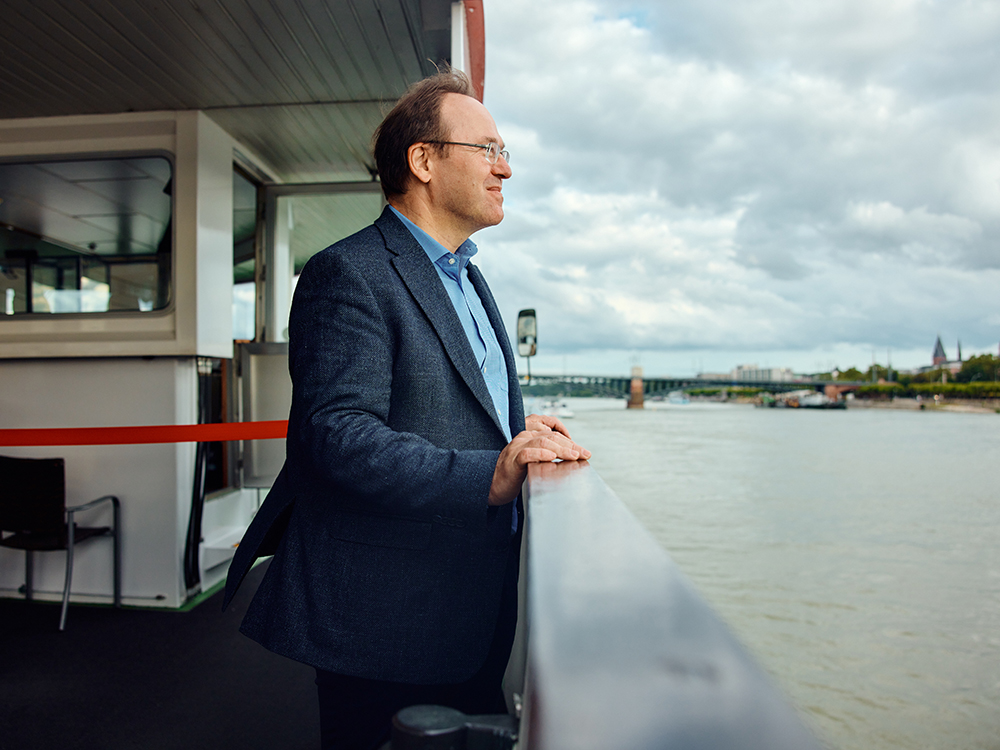 Gewässerökologe Klement Tockner steht an der Reling des Rheindampfers und schaut auf den Fluss.