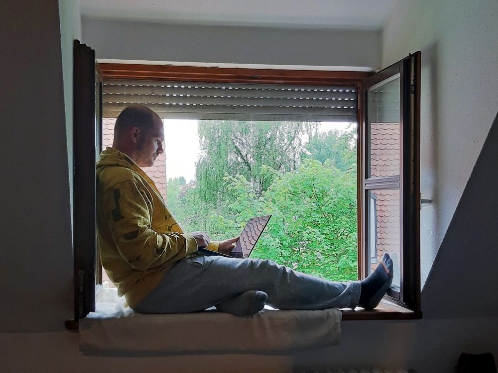 Patrick Marcineck sitzt im Fensterrahmen mit Laptop auf dem Schoß.