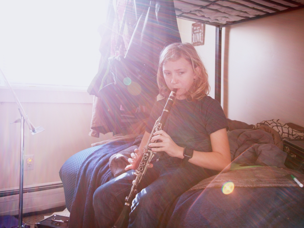Ein Kind sitzt auf der unteren Matratze eines Stockbetts und spielt Klarinette.