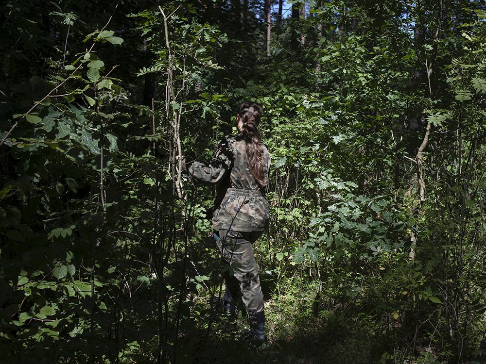 Eine uniformierte Frau geht in einen dichten Wald.