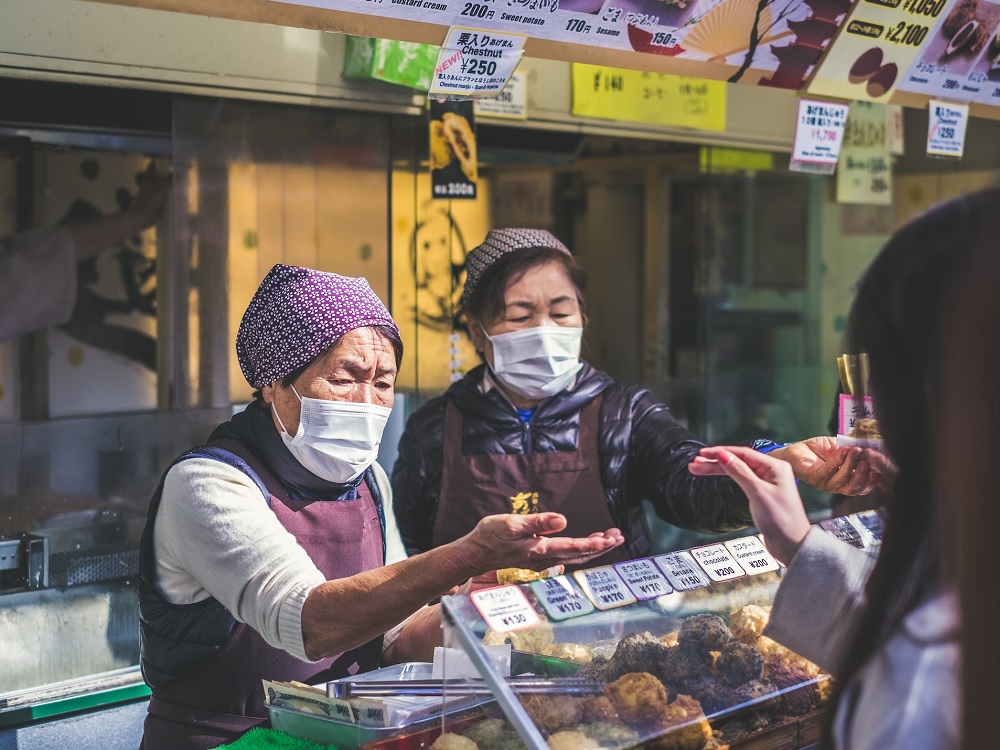 Zwei Japanische Händlerinnen auf einem Marktplatz. Beide tragen Maske